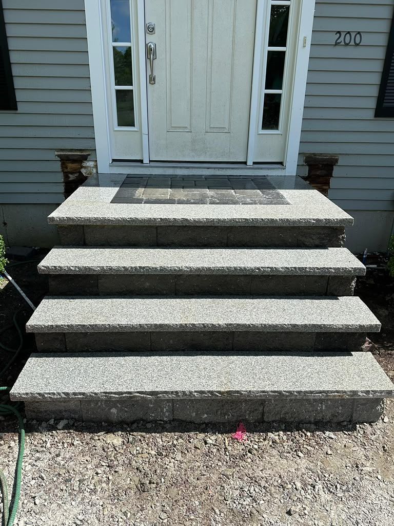 Front porch steps of a house with a white door and side windows, leading up from a gravel path.