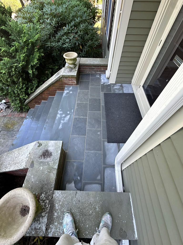 Steep outdoor stone steps beside a house, with a small landing and garden greenery.