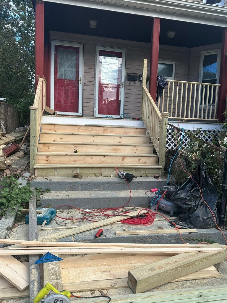 Front porch with red door and new wooden stairs under construction, with lumber and debris below.