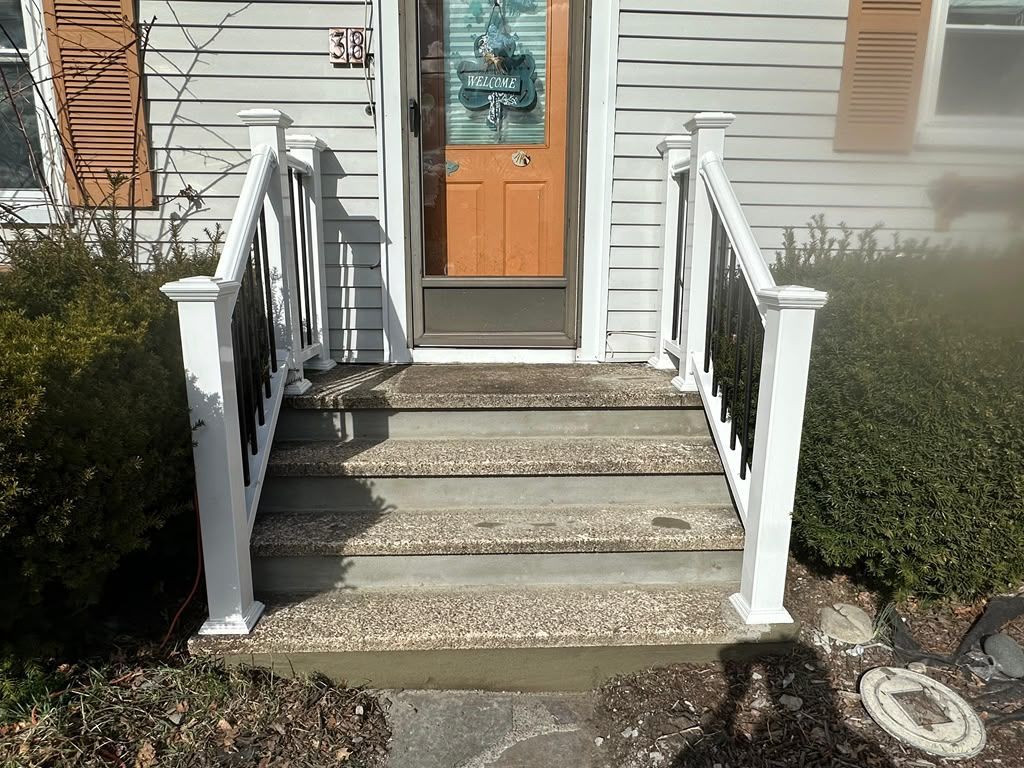 Front steps with white railings leading to a wooden front door on a house exterior