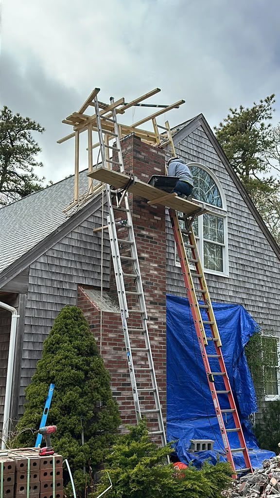 Workers on a roof scaffold over a house, with ladders and blue tarp covering part of the exterior.