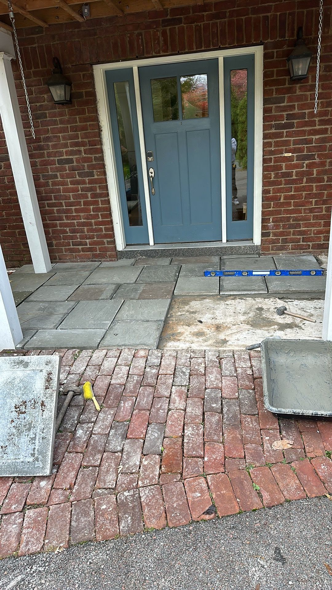 Brick walkway leading to a blue front door with tiled steps and a doormat