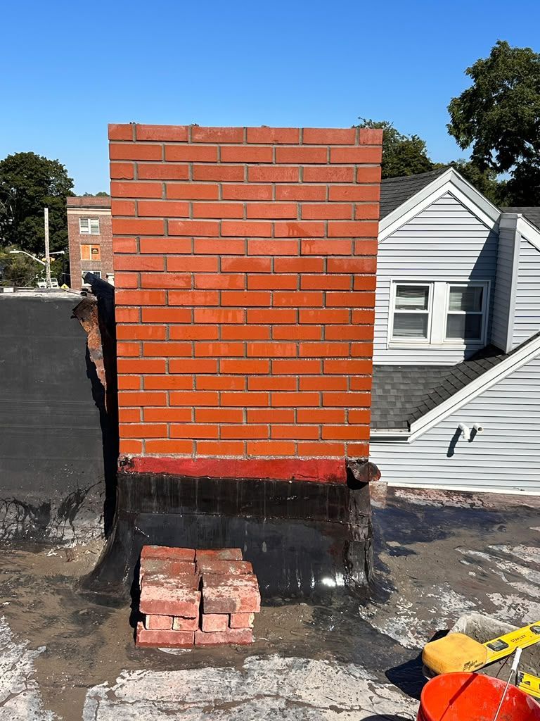 Red brick chimney with black lower section on a rooftop beside neighboring houses.