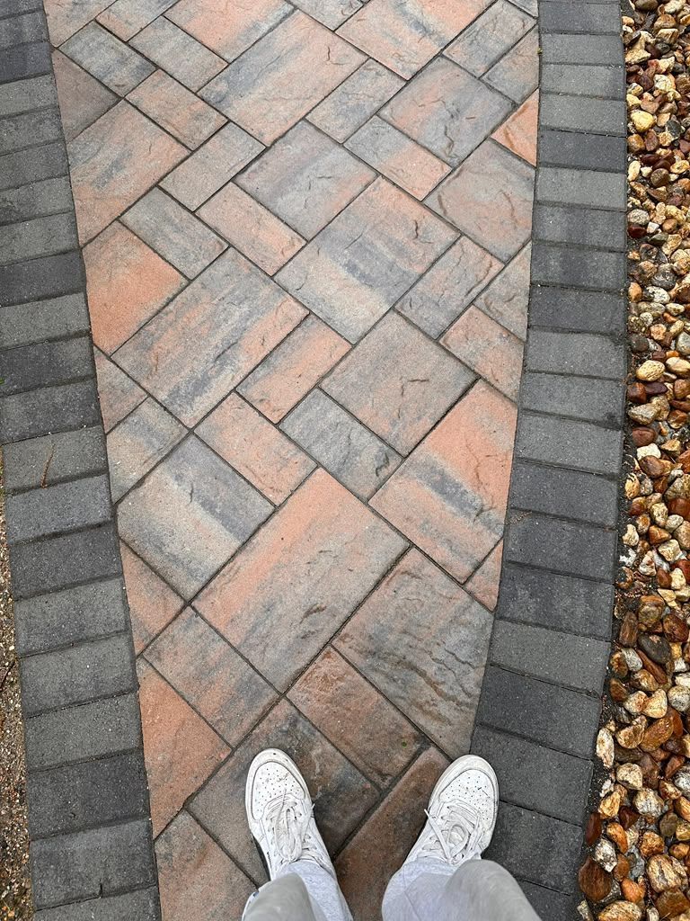 Looking down at white sneakers on a herringbone brick walkway bordered by dark pavers and gravel.