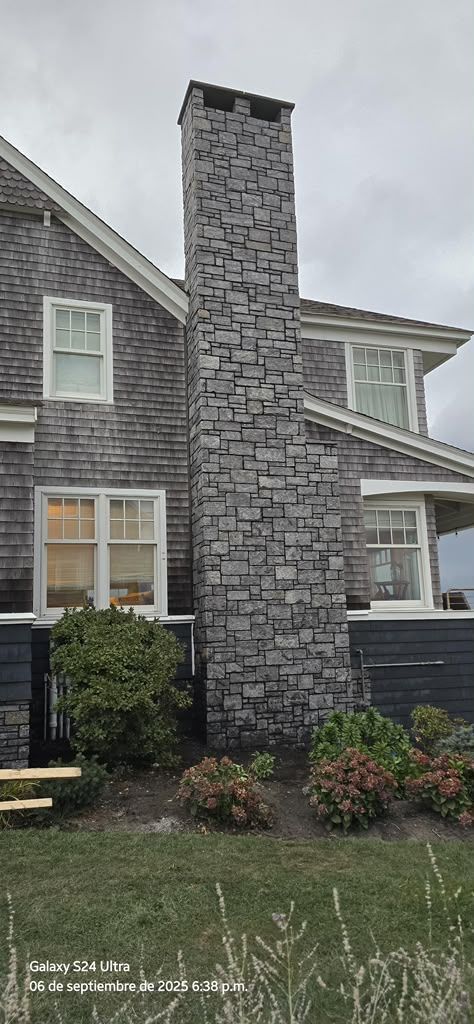 Stone chimney on a gray house with white-trimmed windows and a small front garden.