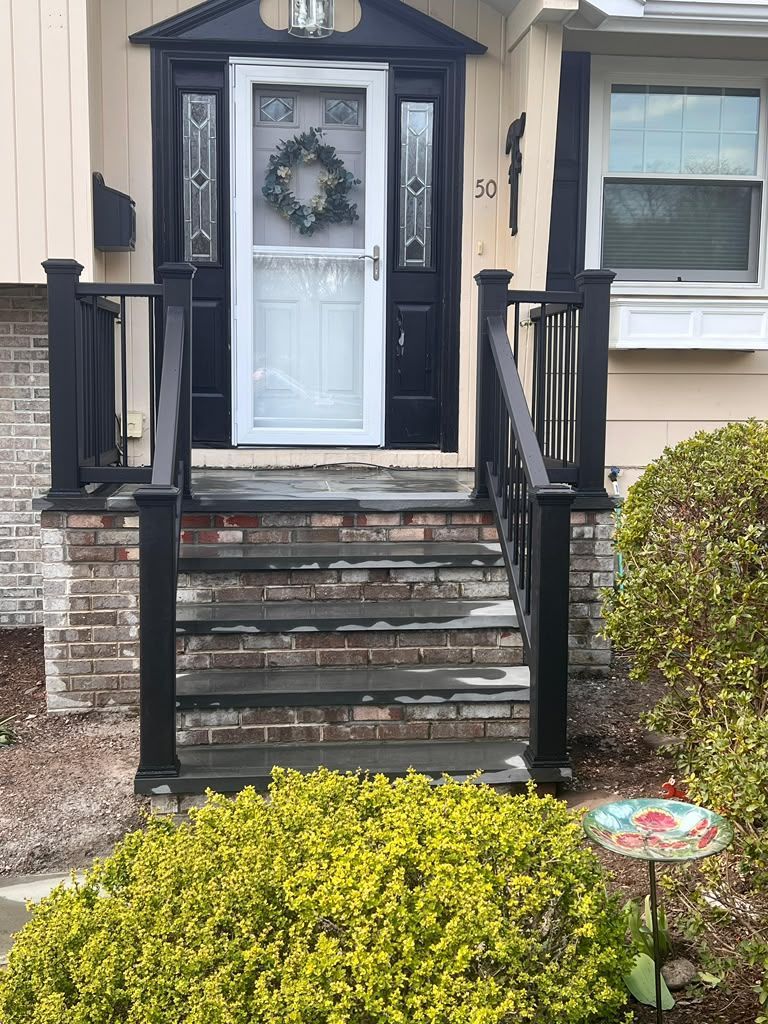 Front porch entrance with black railings, worn steps, white door, and wreath on a beige house.