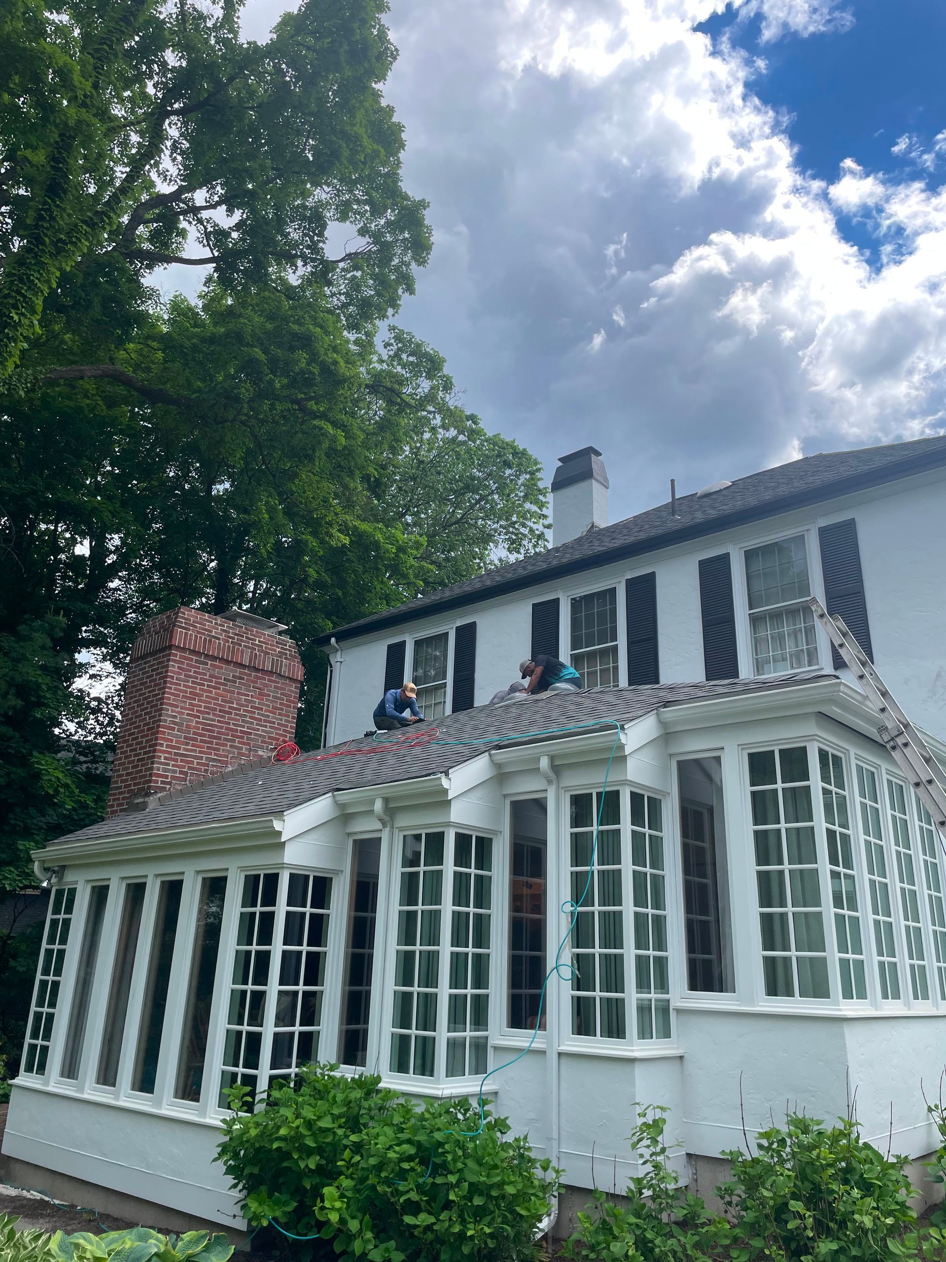 White house with large windows and red brick chimney, partly covered by flowering vines, under a cloudy sky