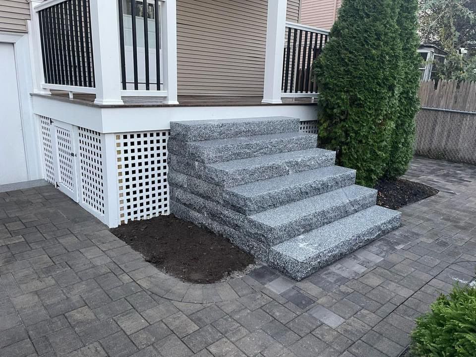Granite front steps leading to a house porch, with paver walkway and shrubs nearby