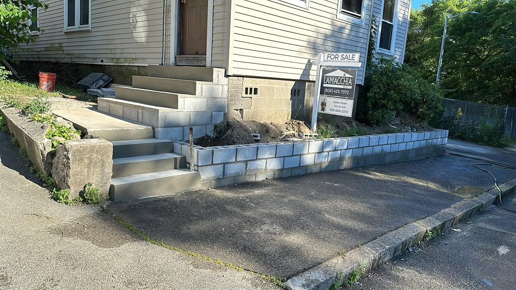 House entrance with concrete steps, retaining wall, driveway, and a real estate sign in front yard