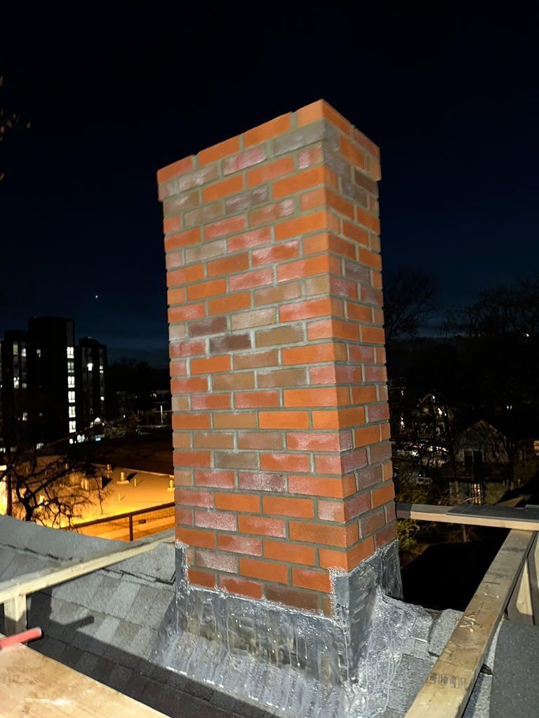 Brick chimney on a rooftop at night, lit against a dark city skyline.