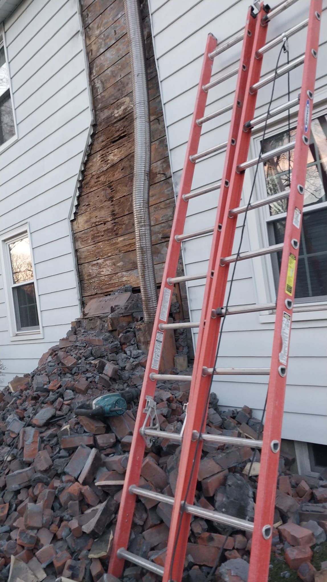 Partially demolished house wall with exposed brick, rubble pile, and red ladders leaning against it