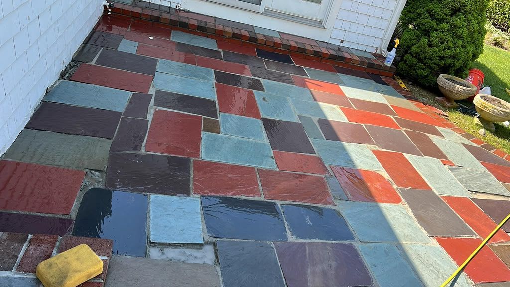 Patchwork of colorful rectangular patio tiles laid in a backyard near a white fence and shed.