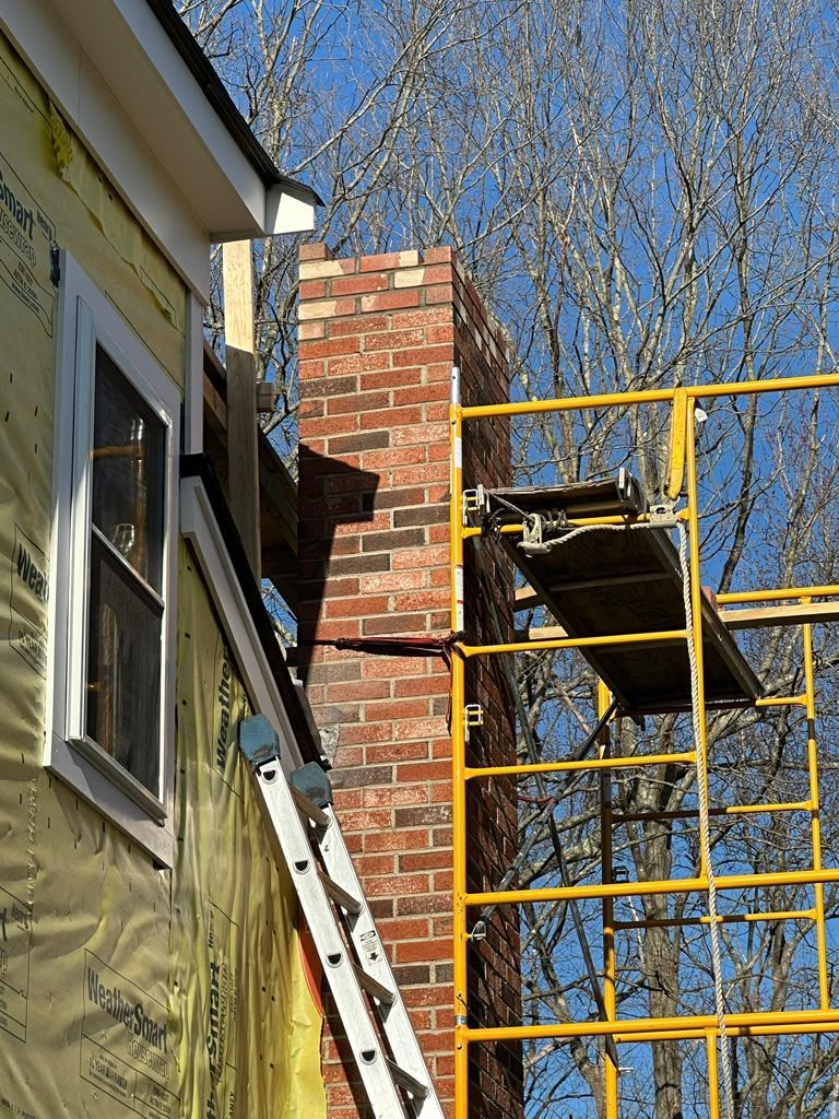 Yellow scaffolding beside a brick chimney and house wall under a clear blue sky