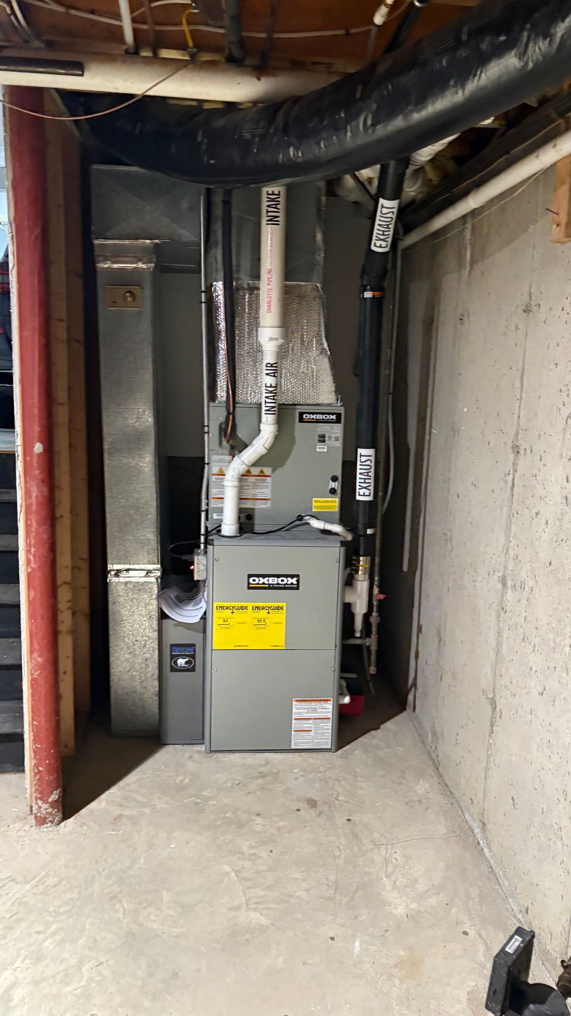 Furnace in a basement setting with ductwork, exhaust pipe, and concrete walls.