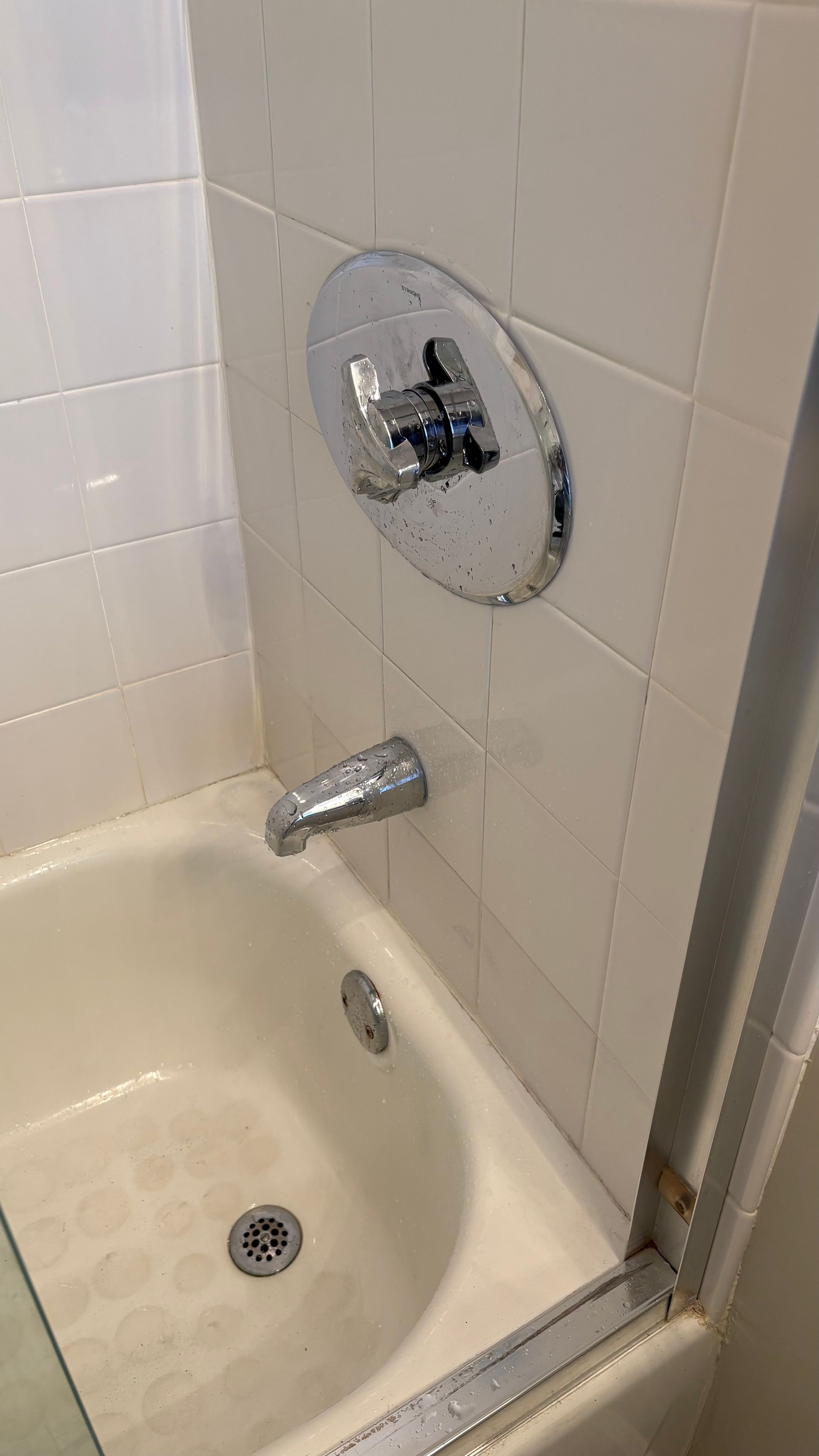 Bathtub with chrome faucet, showerhead, and sliding glass door. White tiled wall.