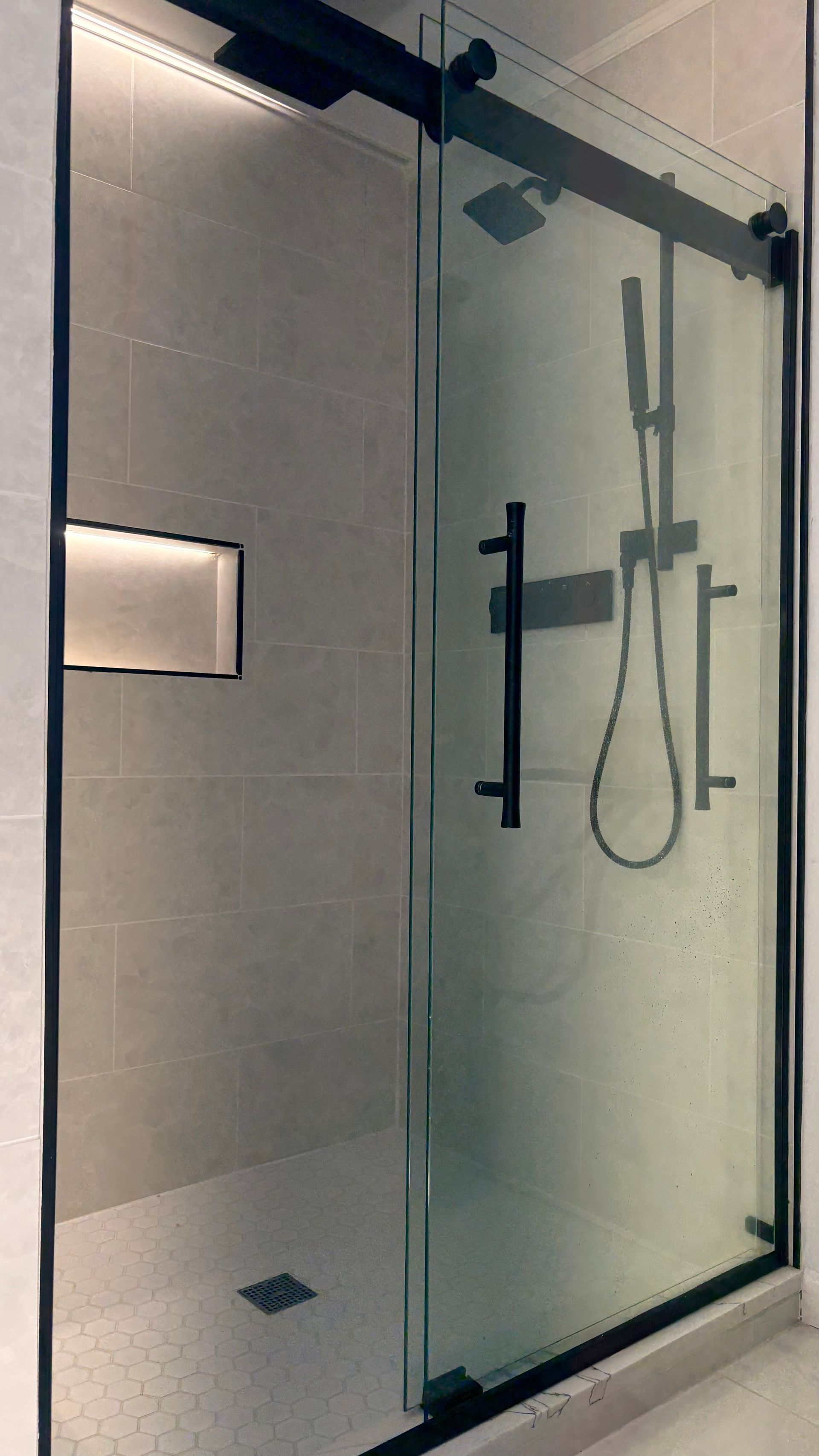 Modern shower with black-framed glass sliding door and black fixtures. Built-in wall niche with lighting.