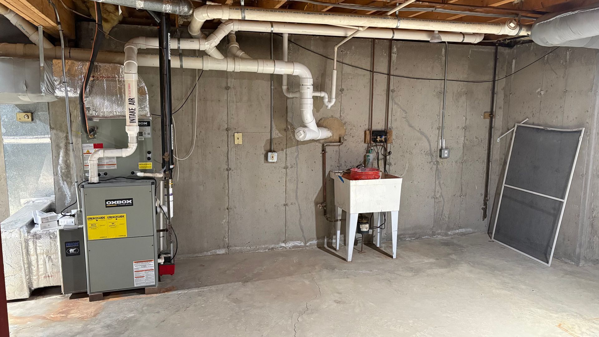Basement with furnace, utility sink, exposed pipes, and concrete walls.