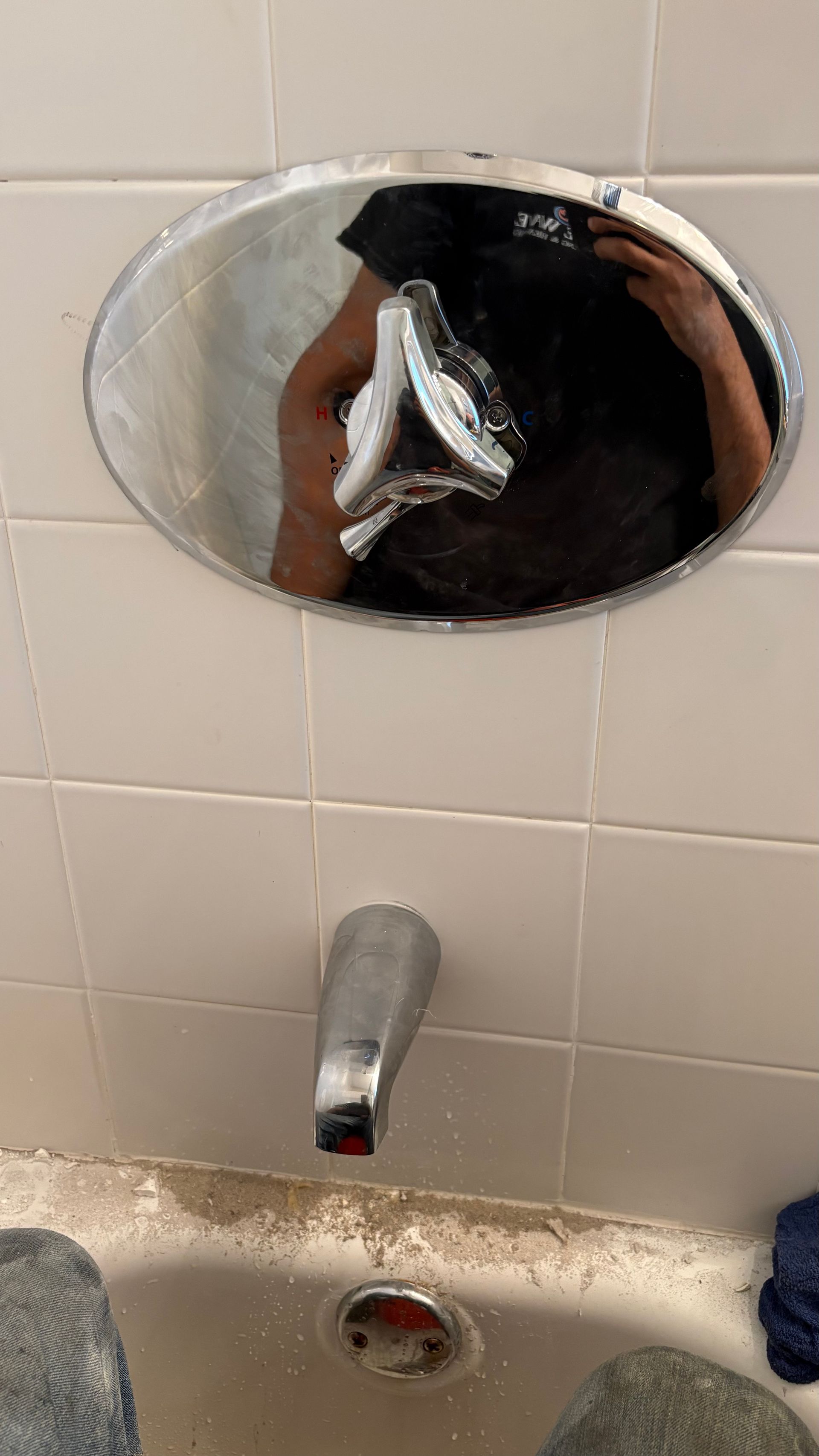 Shower faucet and handle on tiled wall, person reflected in the chrome faceplate.