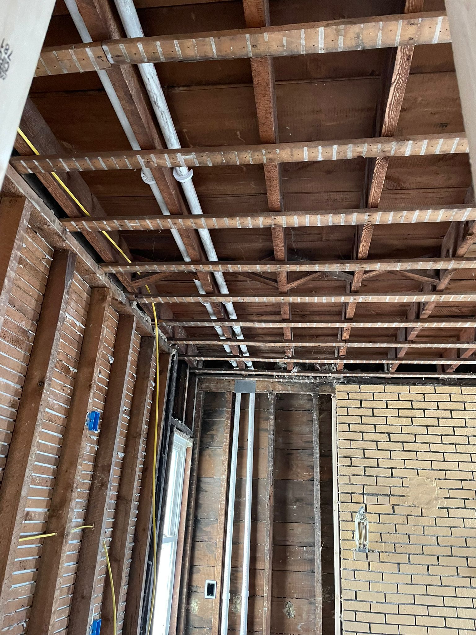 Interior room under construction with exposed wooden framework, pipes, and wiring.