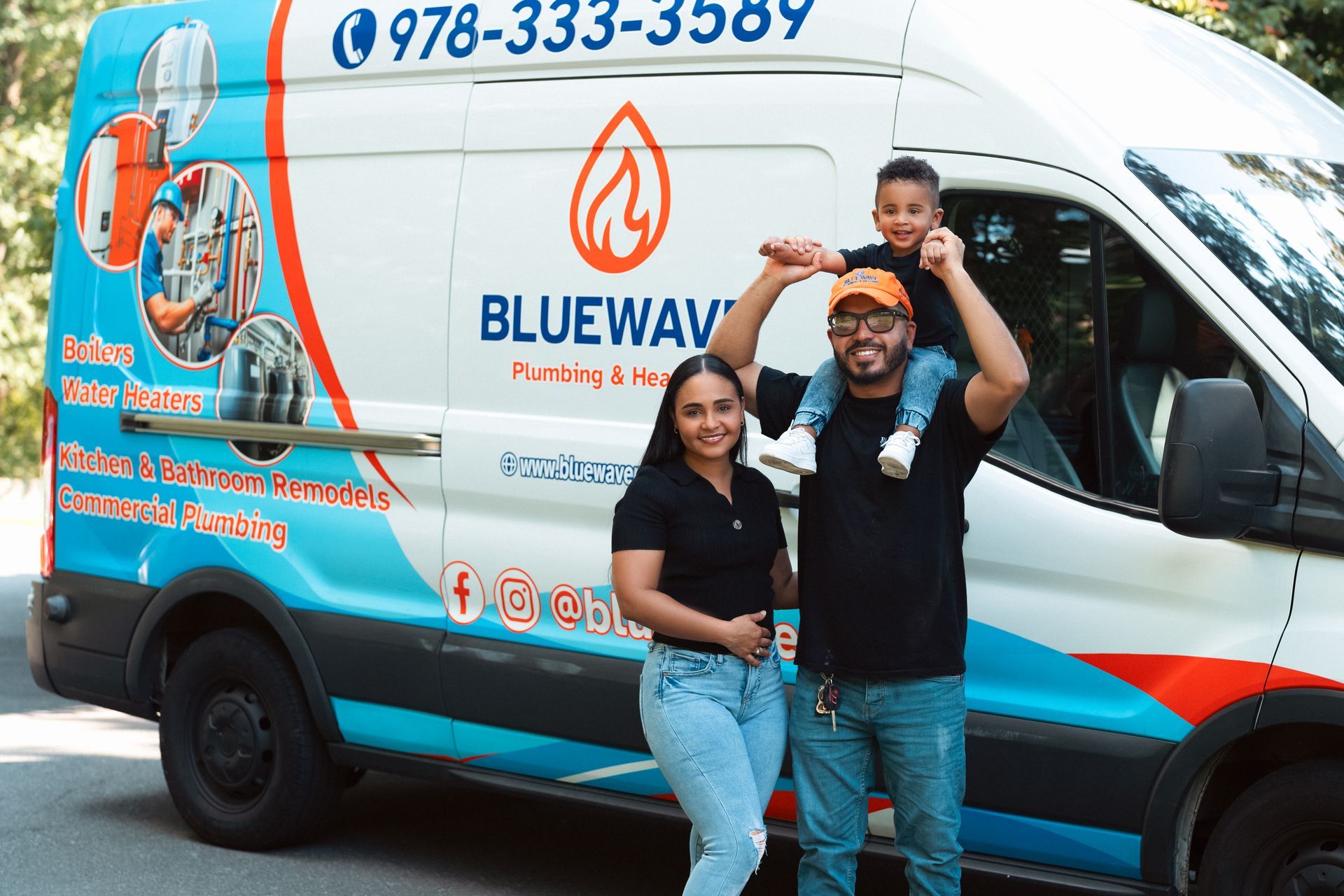 Family posing in front of a Blue Wave Plumbing van. A child is on the father's shoulders.
