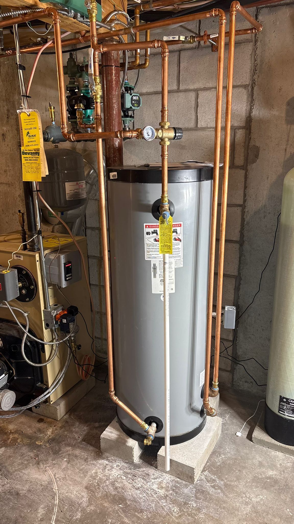 A gray water heater with copper pipes in a basement setting.