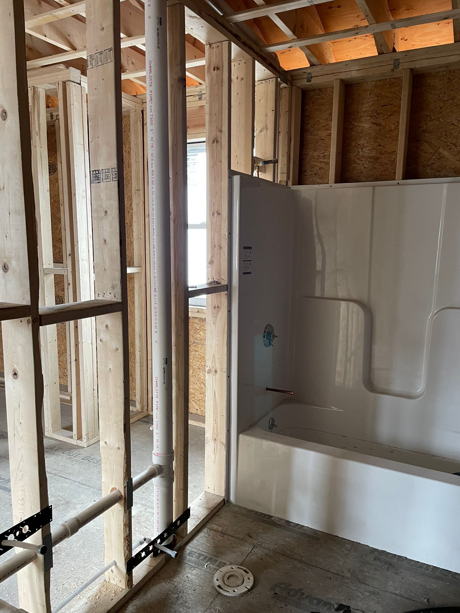 Interior view of a bathroom under construction, showing framing, plumbing, and a white bathtub unit.