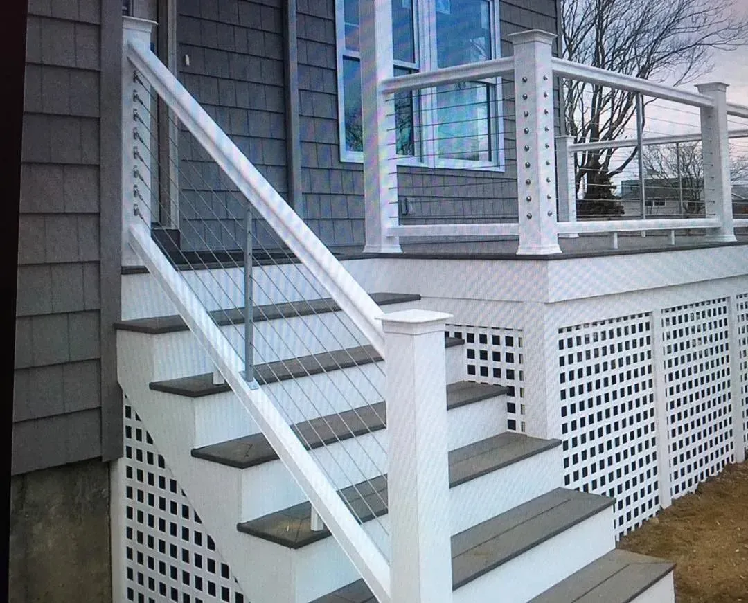 White deck and stairs with cable railing, gray siding, and lattice skirting.