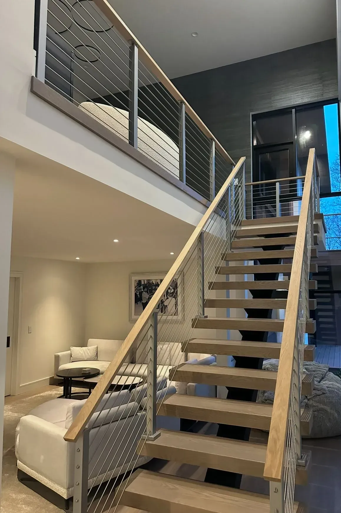 Staircase with wooden steps and stainless steel cable railing in modern home.