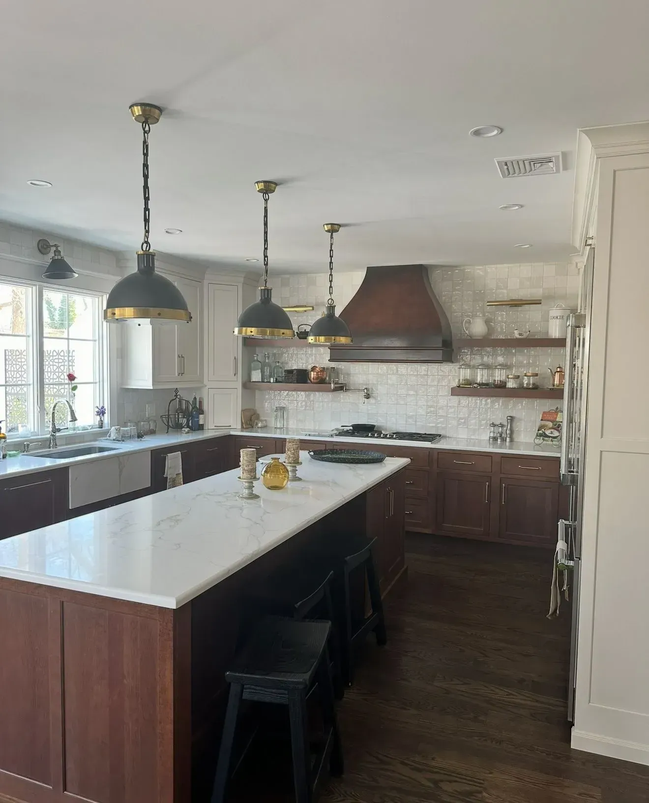 Kitchen with dark wood cabinets, white countertops, and three pendant lights over an island.