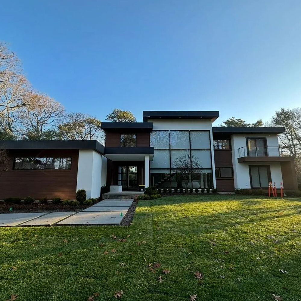 Modern two-story house with brown and white exterior, large windows, and a green lawn.