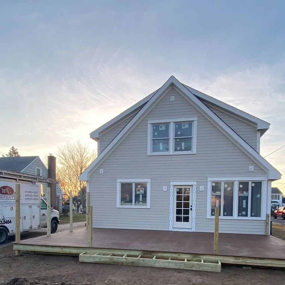 Two-story house with new gray siding and a wooden deck under construction; overcast sky.
