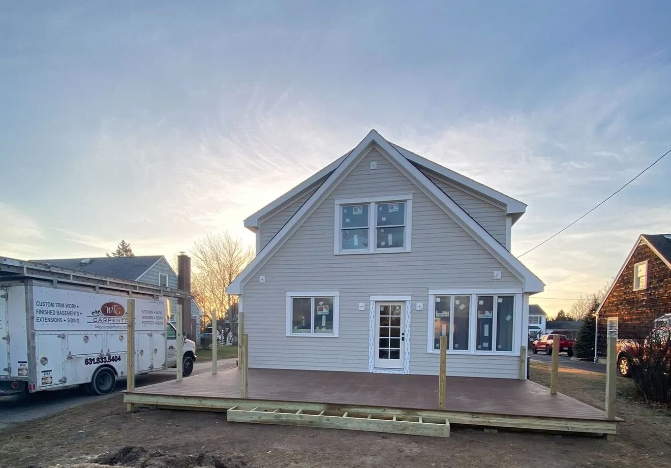 Two-story house with a partially built deck. The sky is bright. A utility truck is parked next to the house.