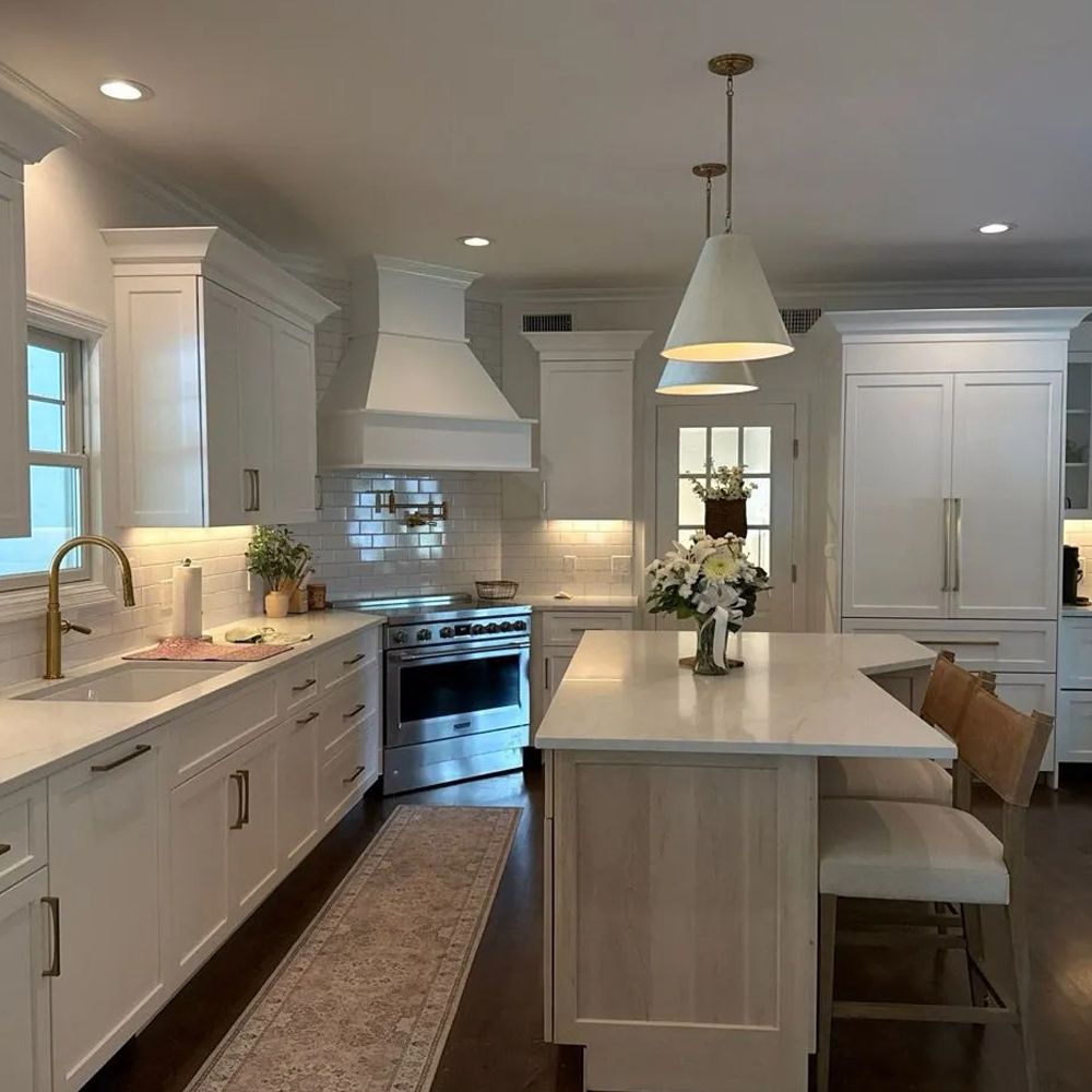 White kitchen with island, range, and cabinets. Light fixtures and floral arrangement.