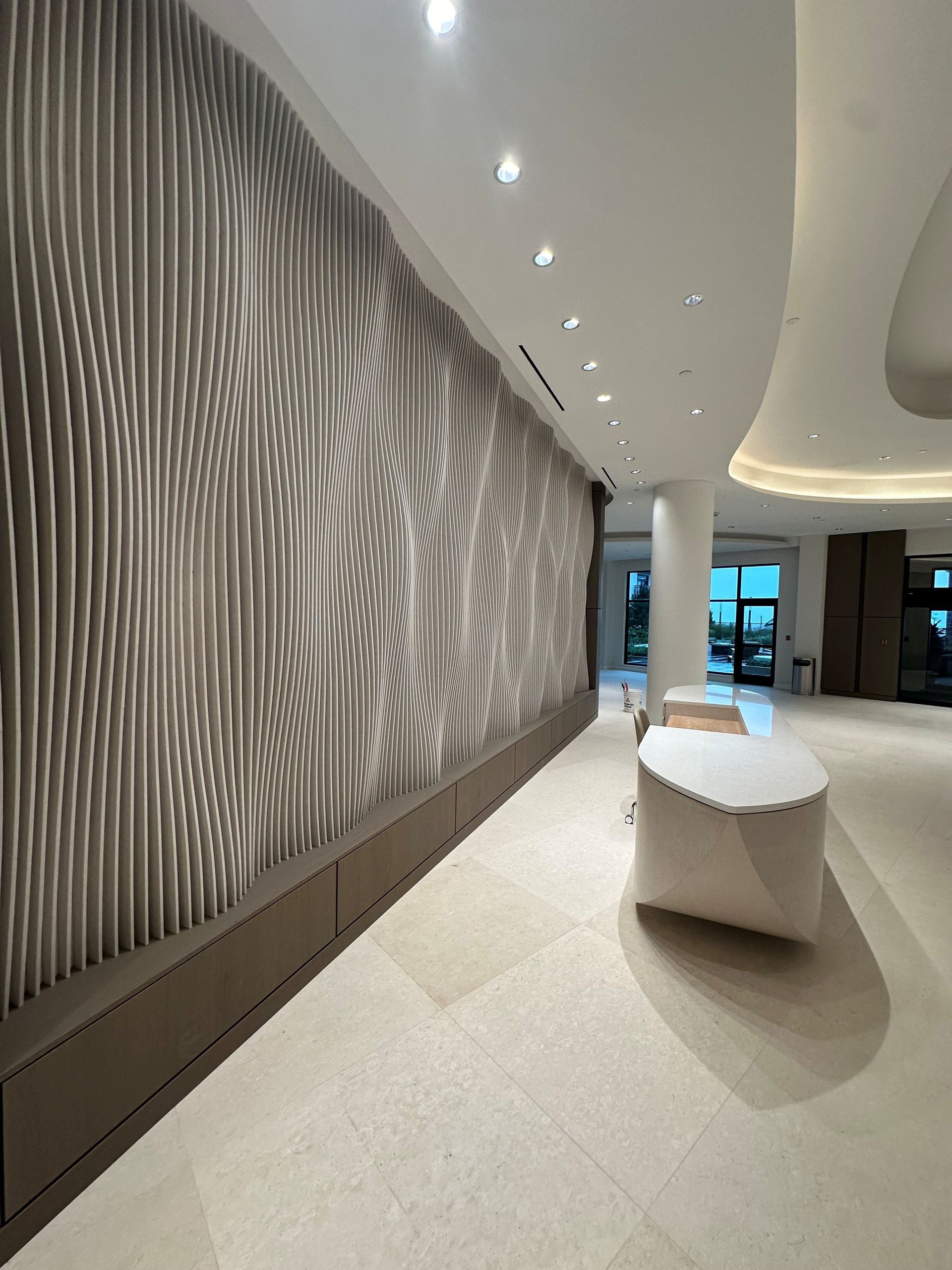 Hallway with large textured wall art. White benches. Bright lighting.