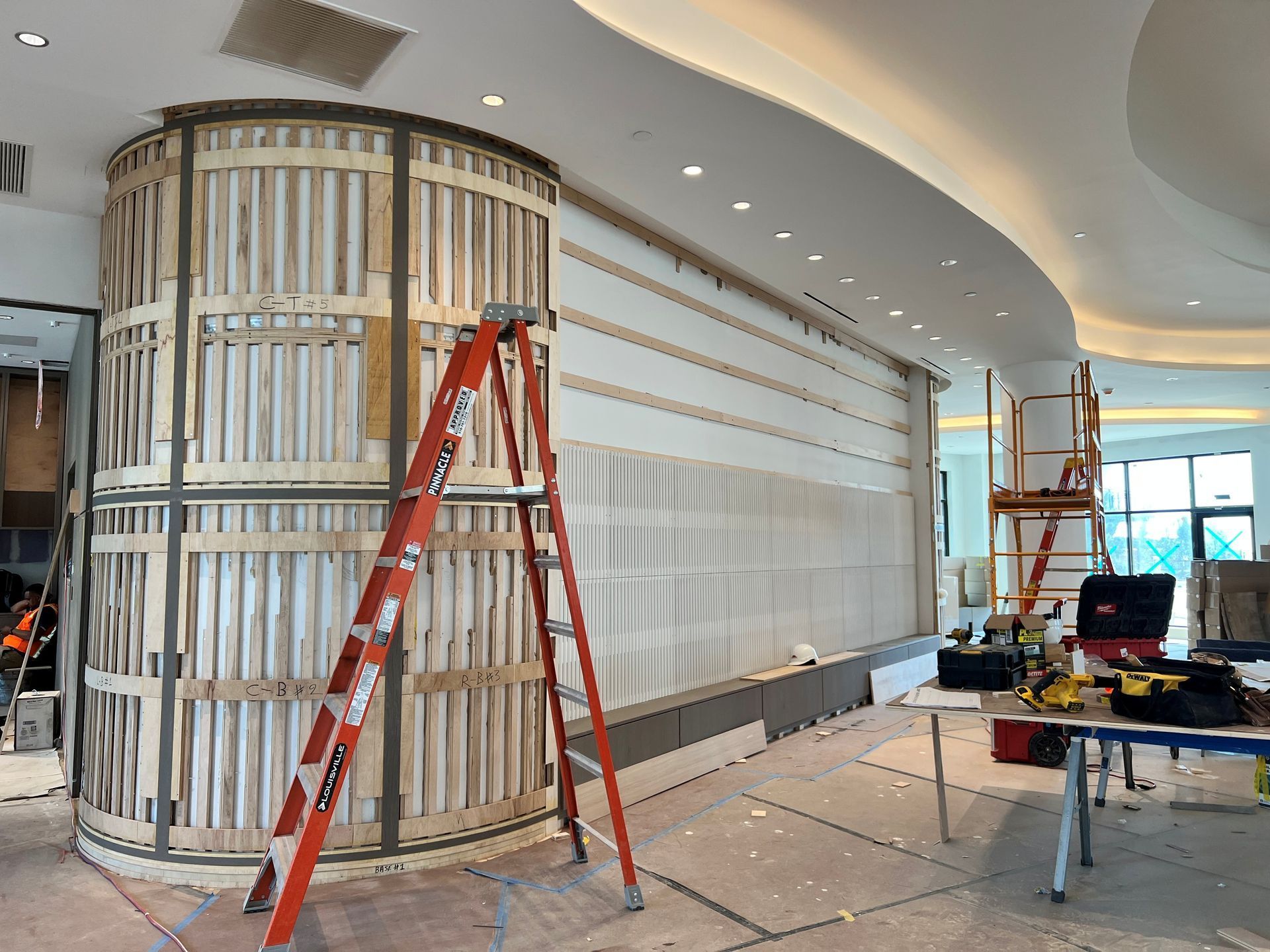 Interior room under construction, with exposed wood framing, insulation, a window, sink, and door.