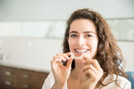 Smiling person holding clear aligners in a bright bathroom