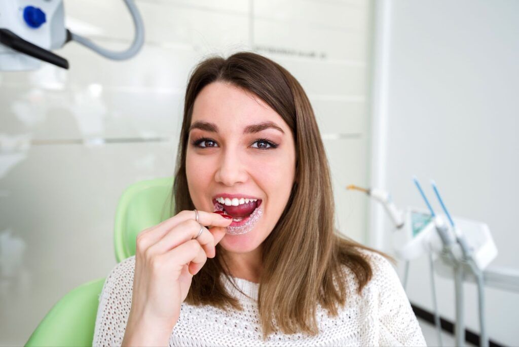 Woman at a dentist’s office holding a dental floss pick and smiling at the camera