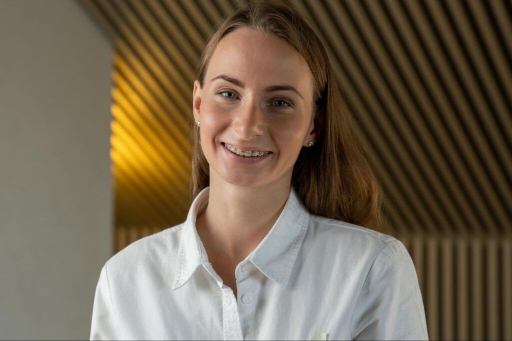Smiling person in a white shirt standing indoors against a warm, striped background