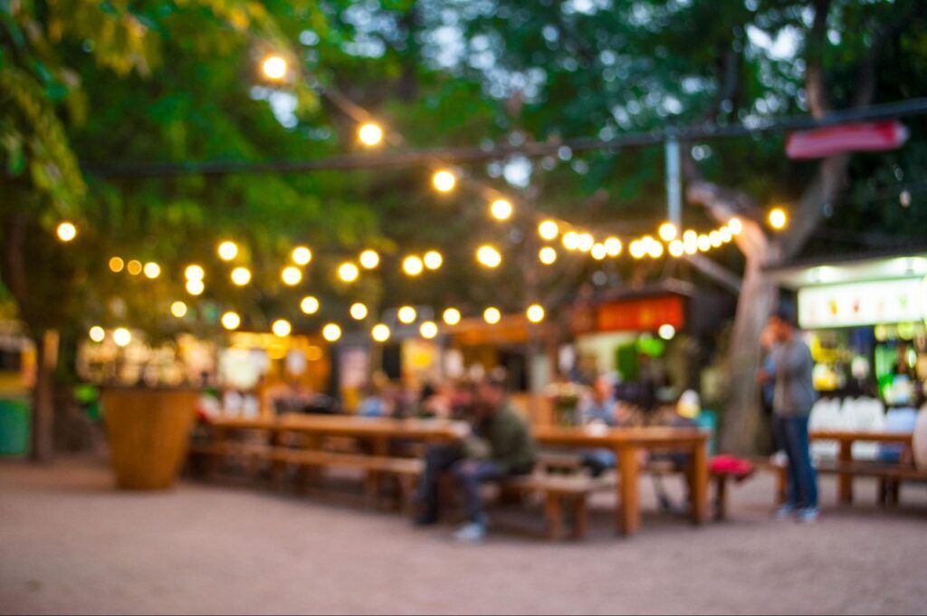 Outdoor café with string lights, wooden tables, and people seated in a lively evening market scene