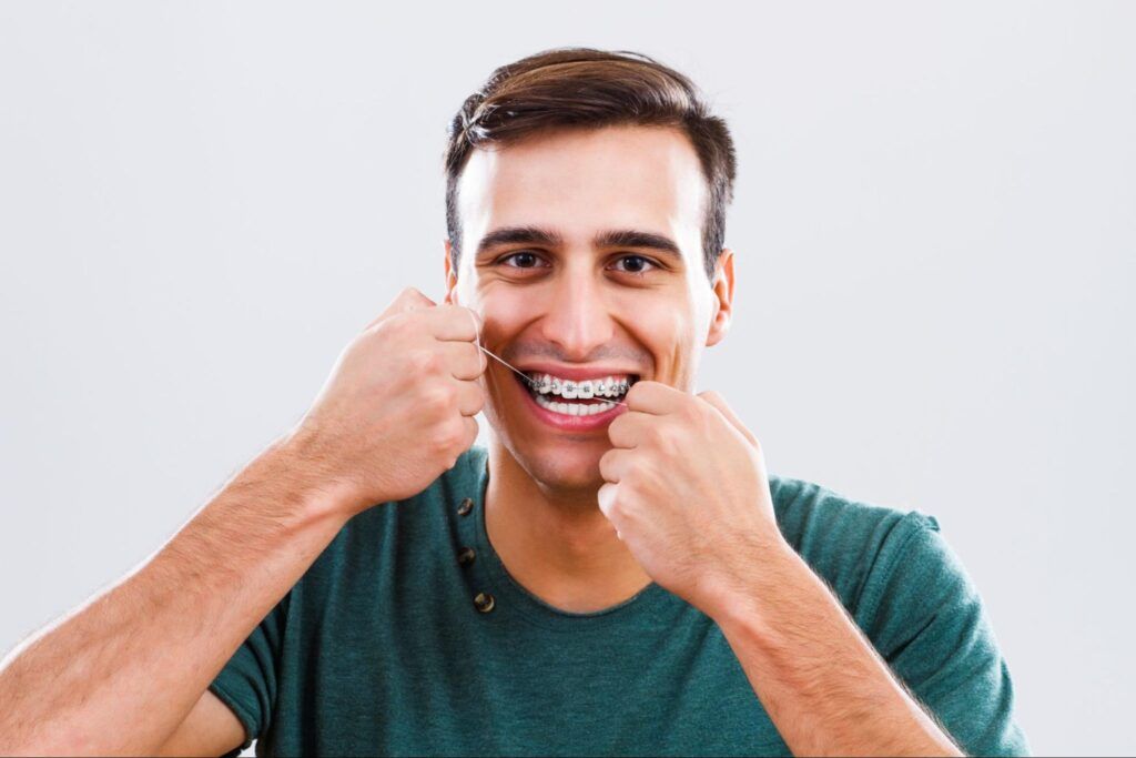 Man smiling while flossing his teeth against a light background