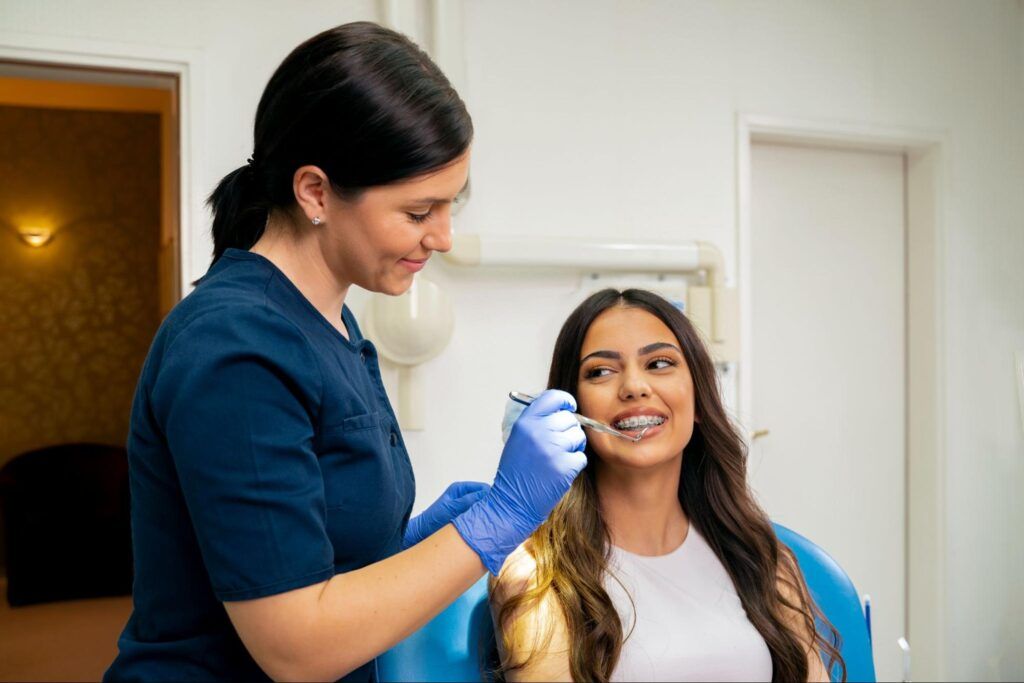 Dental professional examining a smiling patient in a clinic, wearing gloves and using a dental tool.