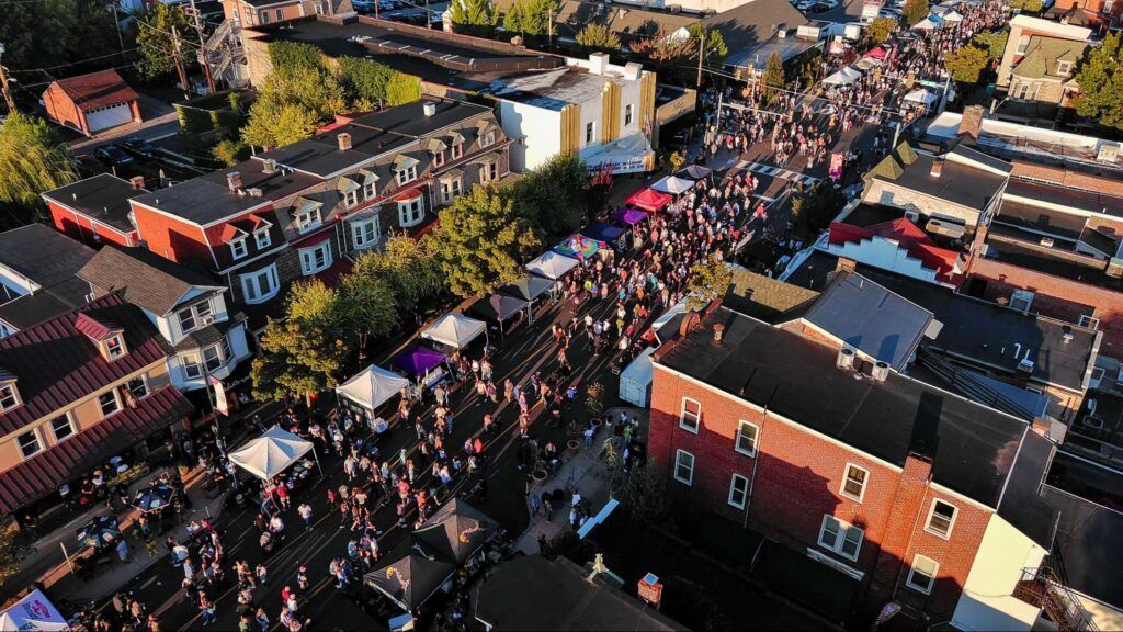 Aerial view of a crowded outdoor street market with colorful stalls between brick buildings.