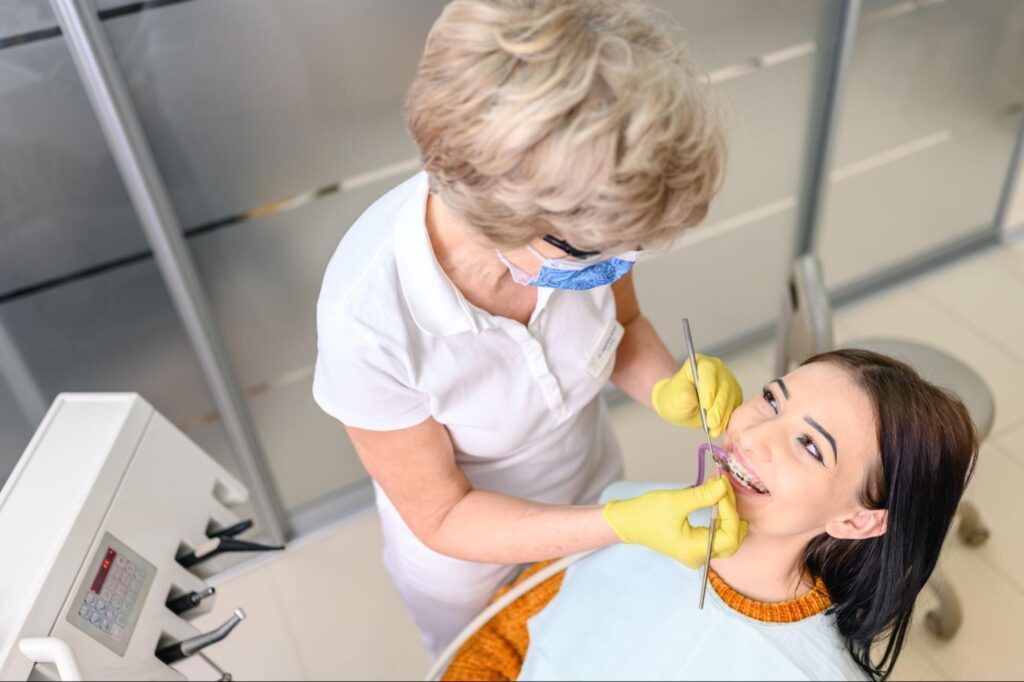 Dentist examining a patient’s mouth in a clinic, wearing yellow gloves and blue safety glasses.