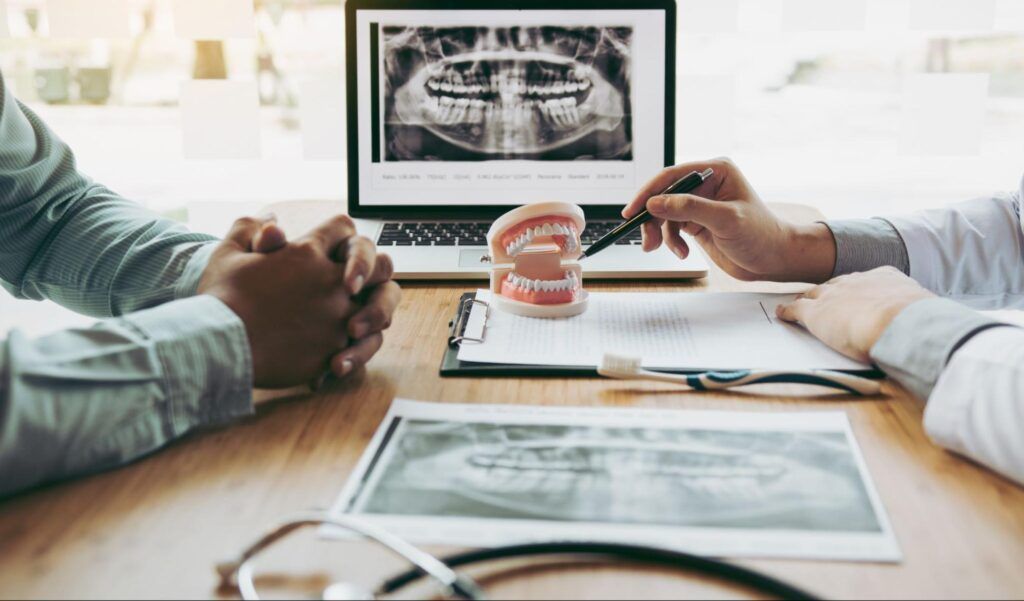 Dental consultation with laptop showing X-ray, dental model, and hands around a table