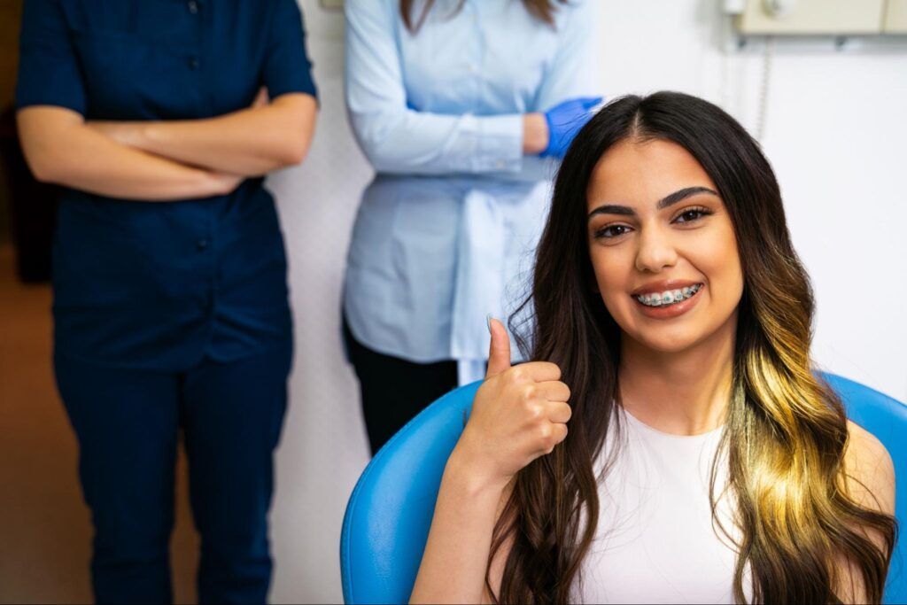Smiling woman giving a thumbs-up in a blue chair, with two people standing behind her