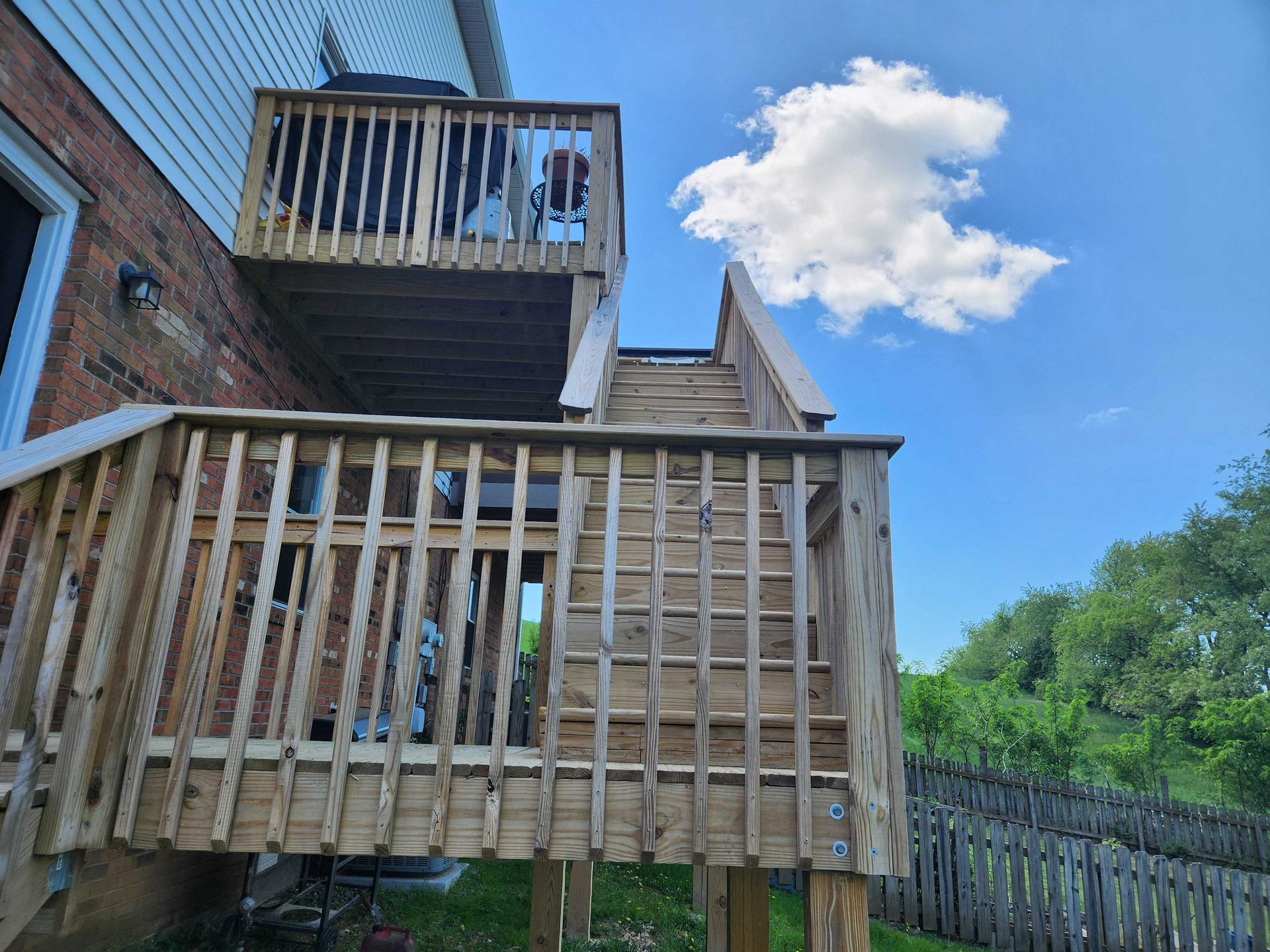 Two-tiered wooden deck with stairs attached to a brick house on a sunny day.