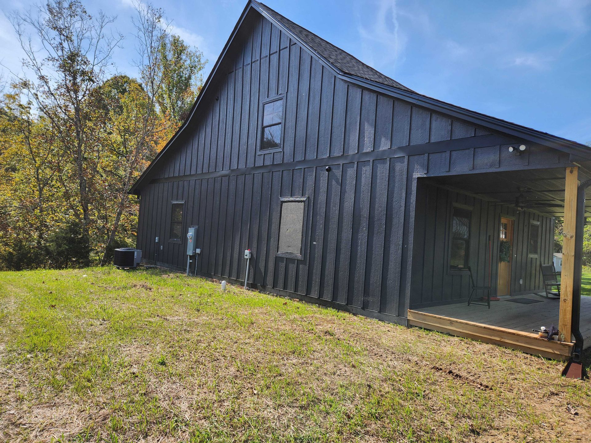 Black house with porch in a grassy field under a blue sky, trees in the background.