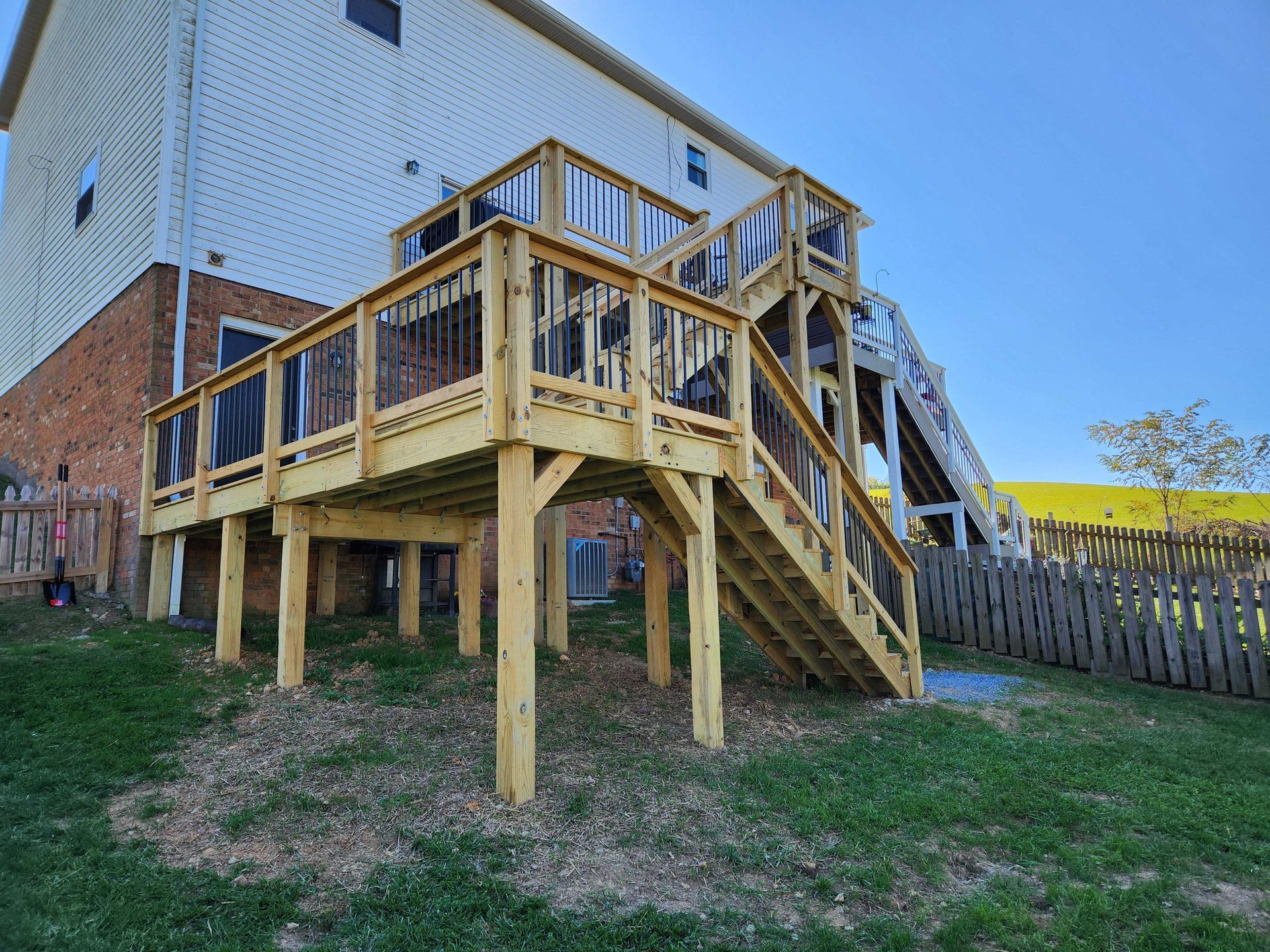 Wooden multi-level deck attached to a brick house, steps leading down, backyard setting.