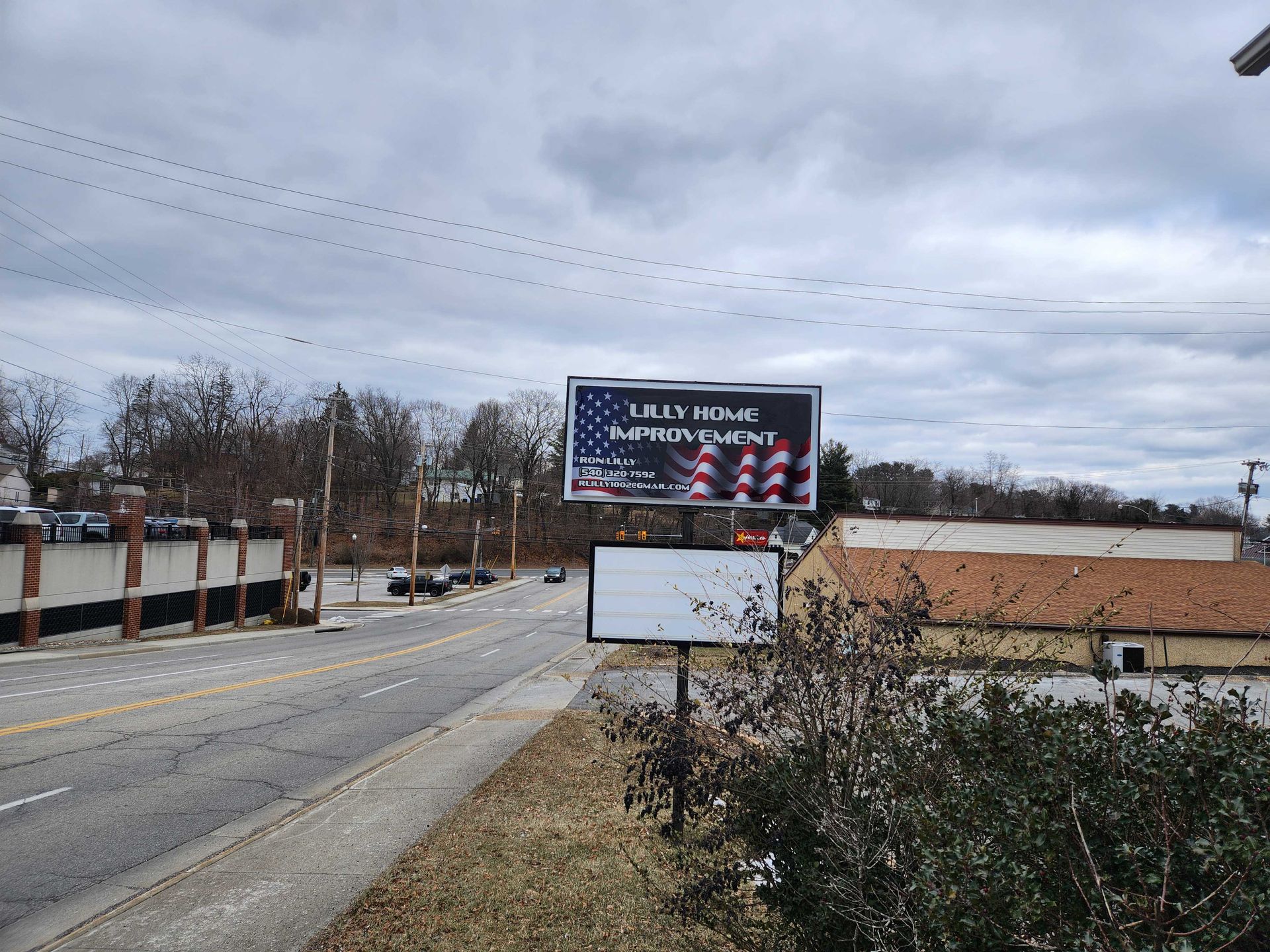 Billboard for a home improvement store, above a blank sign, along a road on a cloudy day.