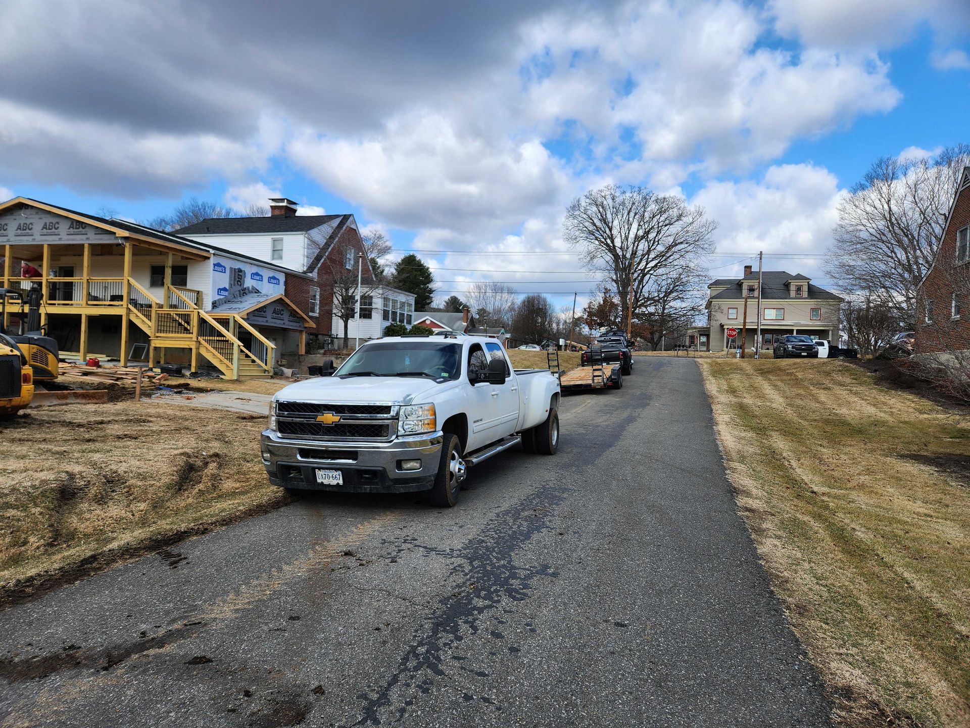 White truck towing a trailer on a narrow road in a residential area. Cloudy sky overhead.